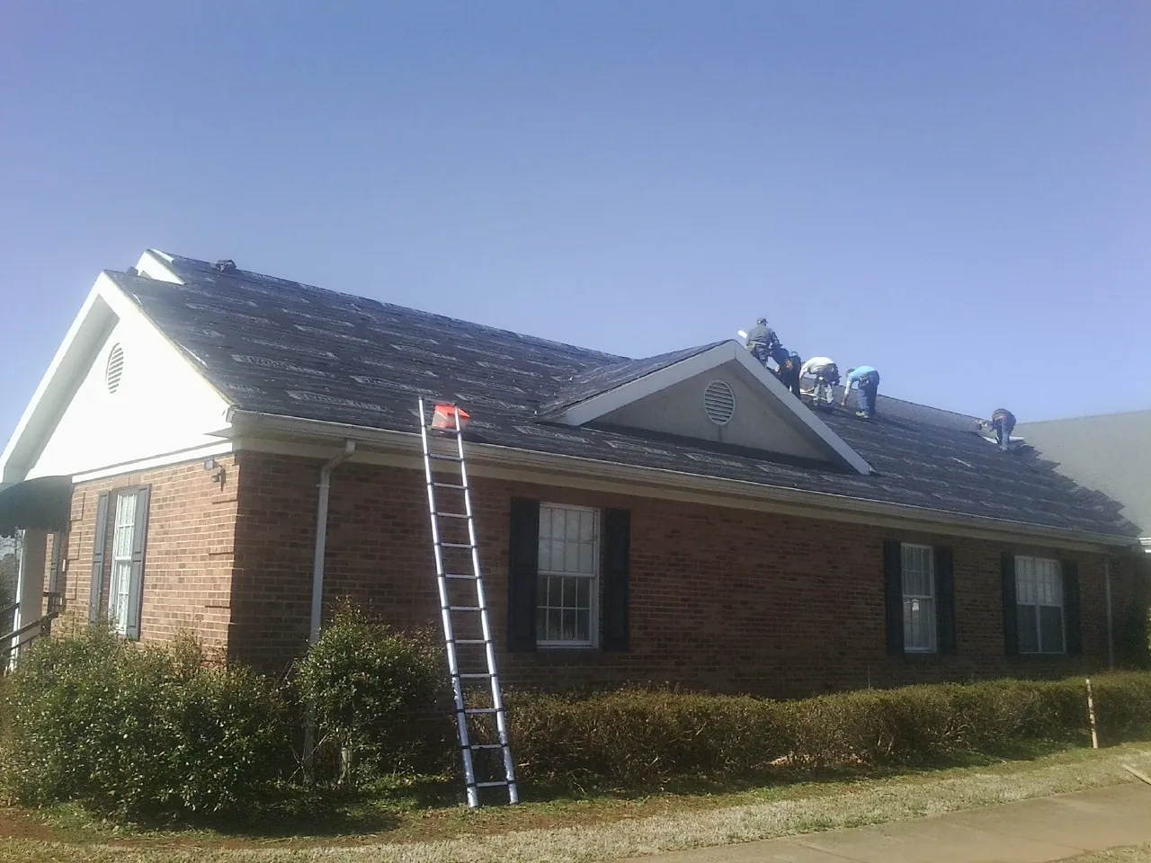 Crew tearing shingles off a brick ranch roof with a ladder set — Metal Roof Repair work by our crew in Norfolk